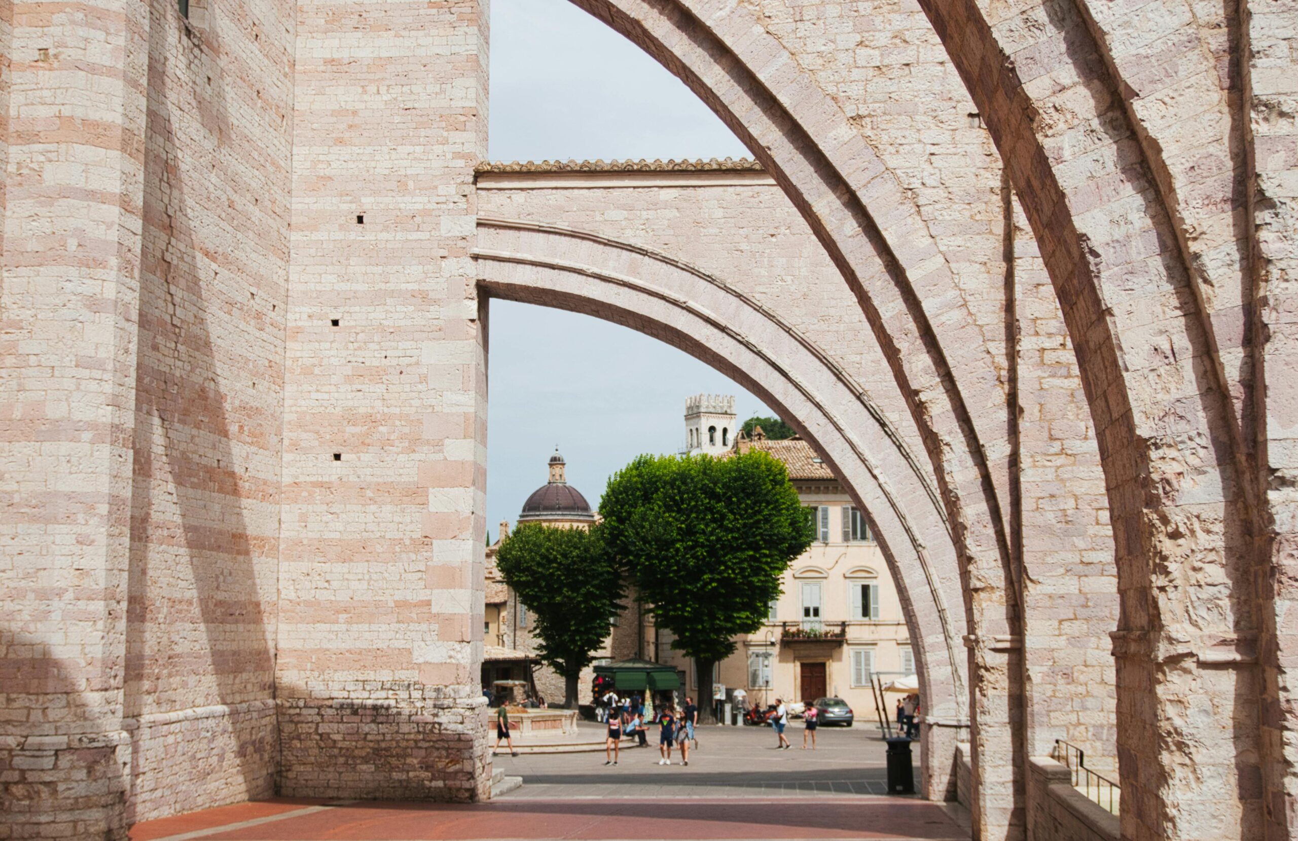 View through stone arches in a European city with people strolling beneath.